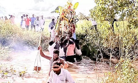 வாய்க்காலில் இறங்கி இறந்தவர் உடலை எடுத்து செல்லும் கிராமமக்கள்.