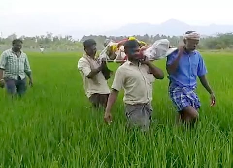 வாடிப்பட்டி அருகே வயல் வெளியில் பிணத்தை தூக்கி செல்கின்றனர்.