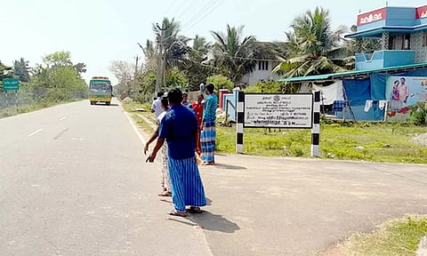 சாலையின் நடுவே பஸ்சுக்காக காத்திருக்கும் பொதுமக்கள்.