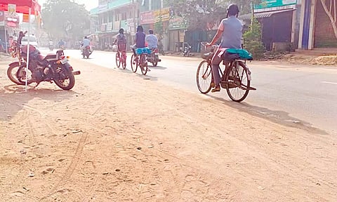 சாலையில் குவிந்துள்ள மணலில் சைக்கிளில் செல்லும் பள்ளி மாணவிகள்.