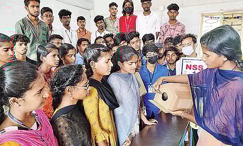 மாணவ,மாணவியர்களுக்கு சிட்டுக் குருவிகளுக்கான செயற்கை கூட்டை உருவாக்கும் விதம் பற்றி விளக்கும் சக மாணவி.