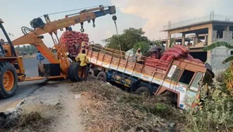 சாலையோர பள்ளத்தில் பாய்ந்த வெங்காய லாரி, கிரேன் மூலம் மீட்கப்படும் காட்சி.