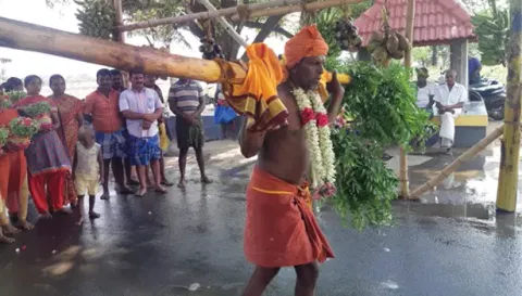 விழாவில், பொது கிணற்றில் விடும் நிகழ்ச்சிக்காக கம்பத்தை பூசாரி தோளில் சுமந்து ஊர்வலமாக சென்ற காட்சி. 