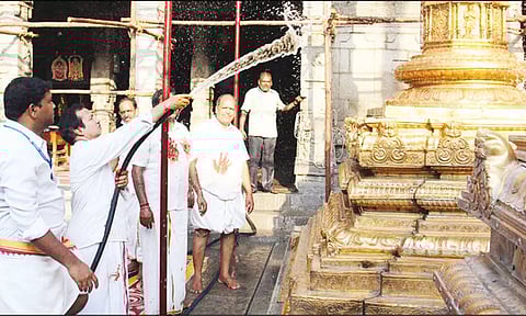 கோவில் அதிகாரி கொடி மரத்துக்கு தண்ணீரை பீய்ச்சியடித்து சுத்தம் செய்த காட்சி.