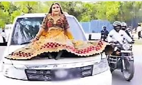 ஓடும் கார் மீது அமைந்து சென்ற இளம்பெண்ணை படத்தில் காணலாம்.