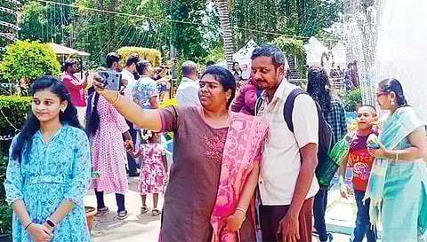 செயற்கை நீரூற்று முன் நின்று செல்பி எடுக்கும் சுற்றுலா பயணிகள்.