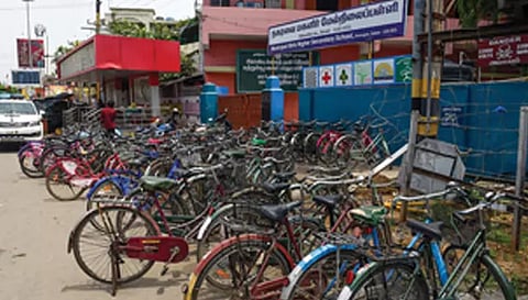 பள்ளி வெளியே சாலை ஓரத்தில் மாணவிகள் சைக்கிள்களை நிறுத்தி உள்ள காட்சி.