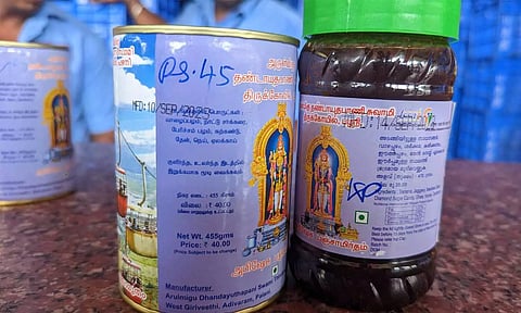 பஞ்சாமிர்த டப்பாக்களில் எம்.ஆர்.பி. விலையை விட அதிக விலையை பேனாவால் எழுதியுள்ள காட்சி.