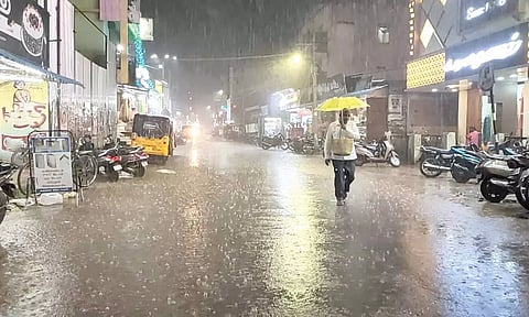 கொட்டும் மழையில் குடை பிடித்தபடி சிரமத்துடன் செல்லும் நபர்.