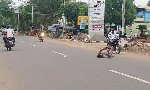 நடுரோட்டில் கால்மேல் கால்போட்டு படுத்து செல்போன் பார்த்த வாலிபர்