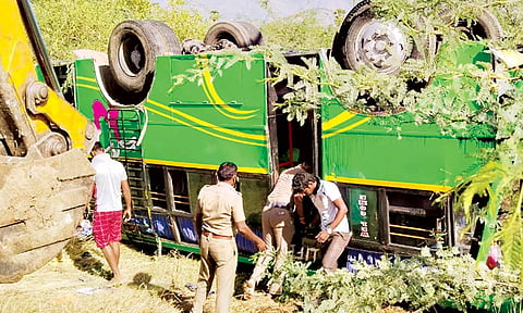 விபத்தில் சிக்கிய மினி பஸ் சாலையோர பள்ளத்தில் தலைகுப்புற கவிழ்ந்து கிடக்கும் காட்சி