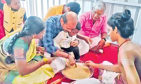தங்களுடைய குழந்தைக்கு நெல்மணிகளைப் பரப்பி எழுத வைத்து வித்யாரம்பம் செய்யும் பெற்றோர்.