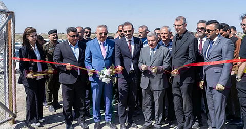 A group of officials in suits and uniforms stand together outdoors, cutting a ceremonial red ribbon to mark the handover of the wastewater treatment project.