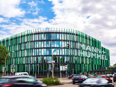 A multi-story modern glass building with vertical green and white louvers forming the MANN+HUMMEL company name on the exterior wall.