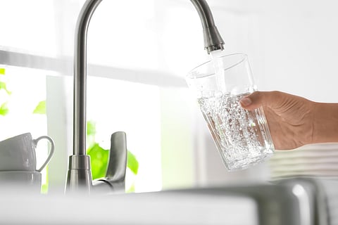 Fresh, clear tap water pouring from a modern curved chrome faucet into a glass held by a hand over a kitchen sink.