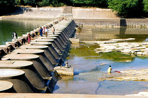 A structural view of a water management system and check-dam in India showing the stark difference between upstream reservoir storage and low downstream water levels during dry summer conditions.