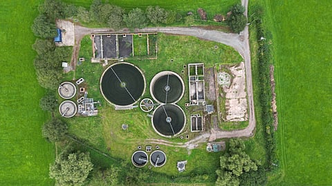 Aerial top-down view of a wastewater treatment plant with circular clarifiers surrounded by green fields