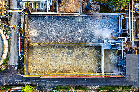 Aerial drone photograph of a modern industrial wastewater treatment plant with rectangular aeration tanks and complex piping networks.