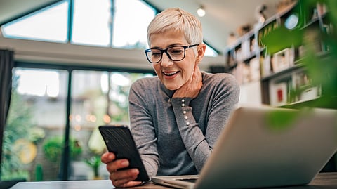 Portrait of a cheerful senior businesswoman using smart phone at home office, close-up.