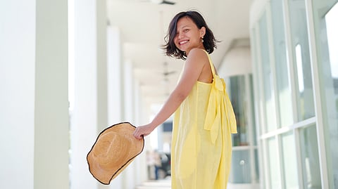 A cheerful solo Asian woman traveler, with a stylish straw hat, looks back with a smile while joyfully exploring Georgetown, Penang