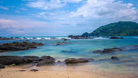Rocky shoreline with turquoise waters and a lush tropical coastline, representing idyllic beach destinations near India.