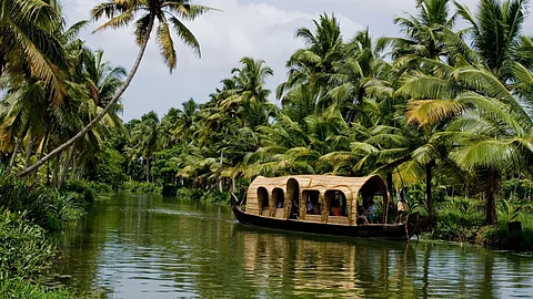 An image of a houseboat on the backwaters of Alleppey in Kerala, amidst lush, green coconut grooves.