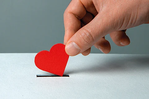 Man’s hand places heart in the donation slot. The concept of the donor of blood or human organs, saving lives