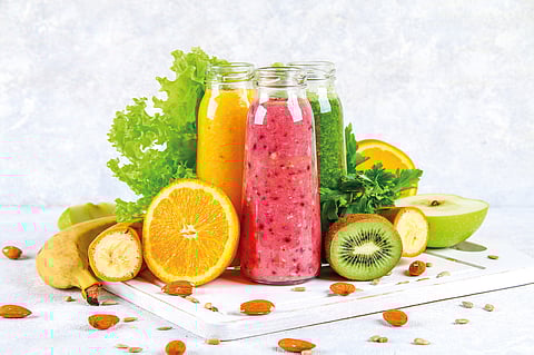 Green, yellow, purple smoothies in currant bottles, parsley, apple, kiwi, orange on a gray table