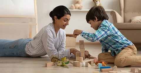 Smiling loving Indian mother and little son playing with toys together, lying on warm wooden floor with underfloor heat, happy young mom and preschool kid having fun at home, building from blocks