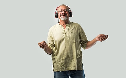 happy senior Indian asian bearded man smiling using headphones with smartphone or tablet against white background, presenting screen or dancing
