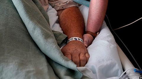 A woman, who is on oxygen as she recovers from COVID-19, holds the hand of her husband, who also contracted COVID-19, as he is kept alive with the help of an oxygenation machine at a medical center in Shreveport (Image Source- VOA)