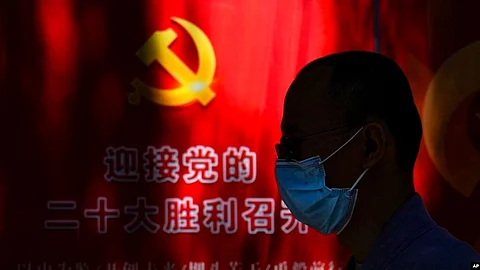 A man wearing a face mask walks by a propaganda poster welcoming the 20th party congress, along a street in Beijing, Sept. 20, 2022. (Image source-VOA)