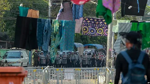 An anti-coup protester stands behind a line of women's clothing hung across a road to deter security personnel from closing in, in Yangon, Myanmar