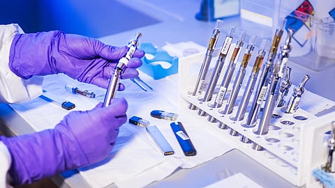 A person wearing a lab coat is holding medical instruments, highlighting the importance of clinical trials in research.