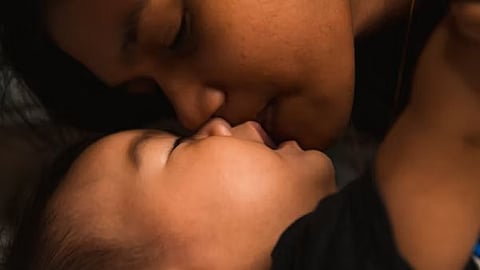 A woman lovingly kisses her baby while lying on a bed, showcasing a tender moment of affection.
