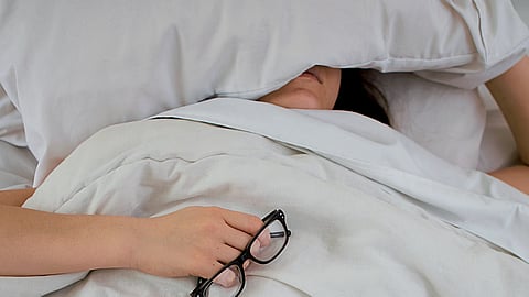 A person lying in bed wearing glasses, appearing relaxed and comfortable.