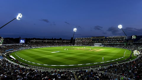 A panoramic view of the cricket stadium illuminated during the evening, showcasing the field and surrounding stands.