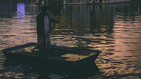 A man in a boat on the water, with a building visible in the background.