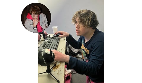 Norme wearing a pink shirt is seated at a computer, engaged in work or browsing.