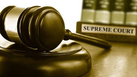 A judge's gavel on its sounding block on a wooden desk with a board showing supreme court.