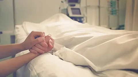 A by-stander holding the hand of a patient in bed.