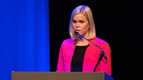 A picture of a woman in pink blazer speaking in a public event.