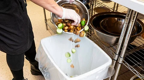 A person throwing away some raw vegetables to a garbage bin.