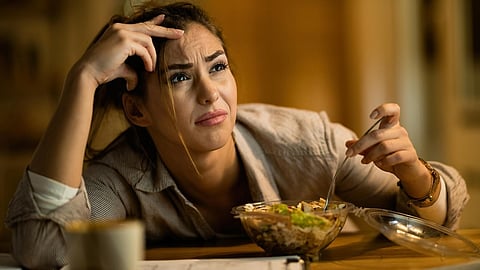 Woman with a stressed expression, holding a fork during a meal.