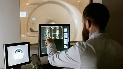 A man in a white coat examines a computer screen, focused on the information displayed.