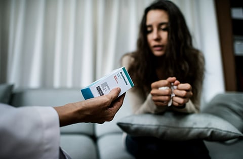 A woman seated on a couch examines a prescription card, appearing contemplative about her medication.
