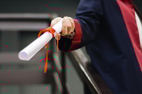 A person wearing a graduation robe stands with a diploma in hand