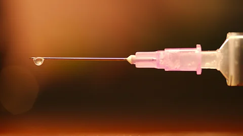 A drop is dropping from the tip of the syringe.