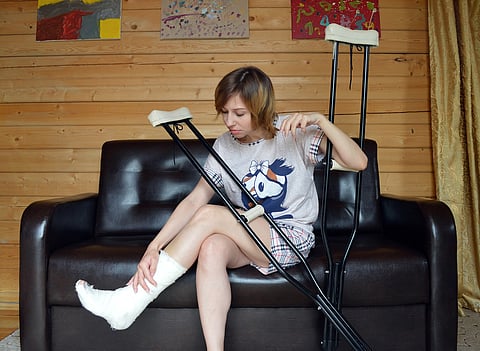 A woman seated on a couch, crutches leaning against her, and looking pensive.