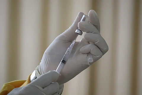 A person dressed in a yellow jacket and white gloves is poised with a syringe, suggesting a healthcare setting.